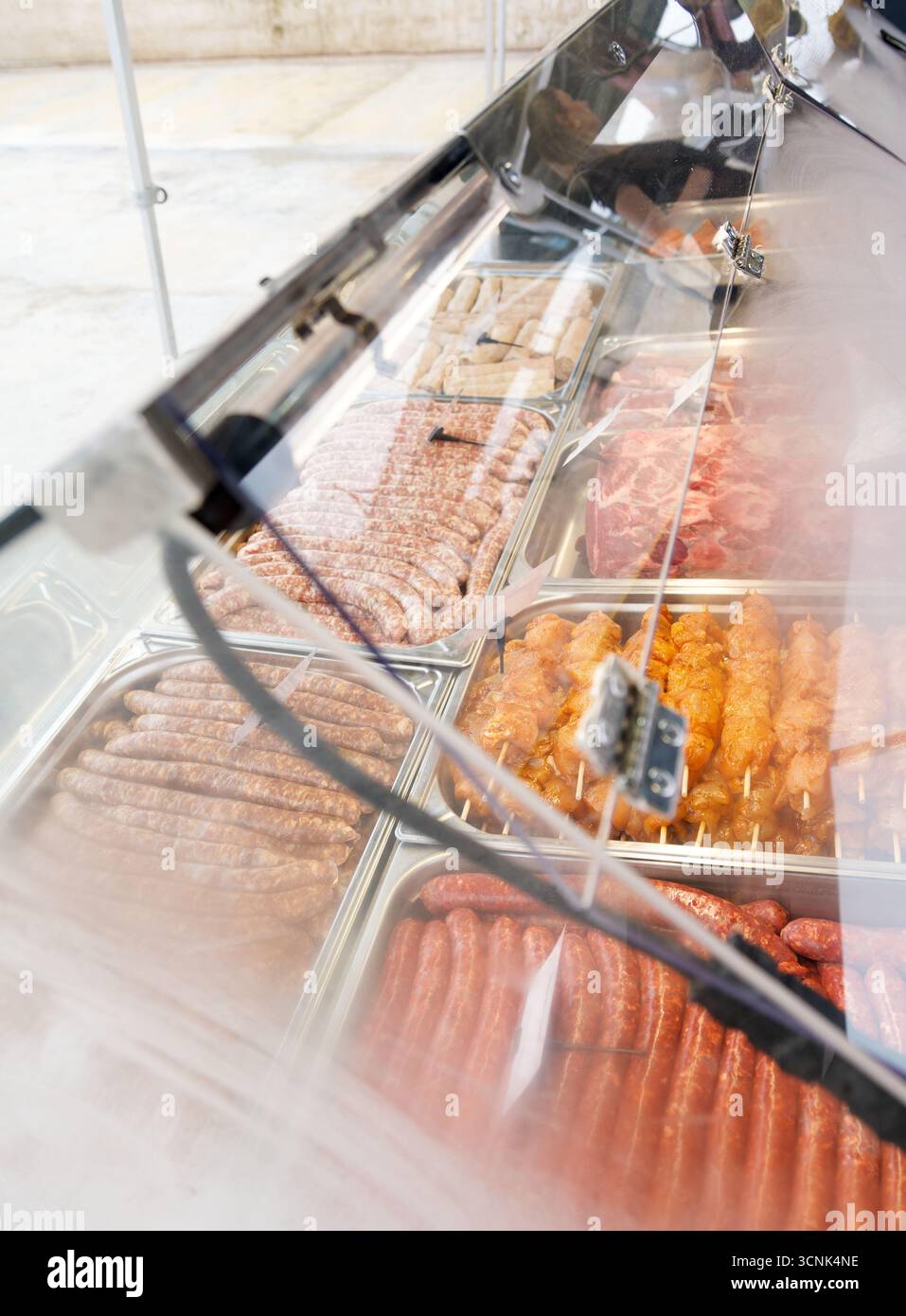 Rohe Fleischgerichte und marinierte Spieße werden in einer Kühltheke bei einer festlichen Familienfeier oder Grillveranstaltung präsentiert. Stockfoto