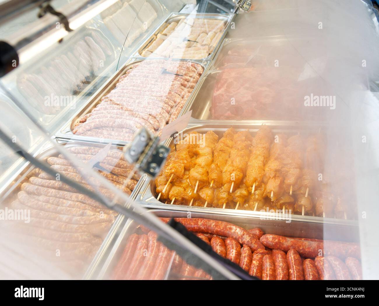 Rohe Fleischgerichte und marinierte Spieße werden in einer Kühltheke bei einer festlichen Familienfeier oder Grillveranstaltung präsentiert. Stockfoto