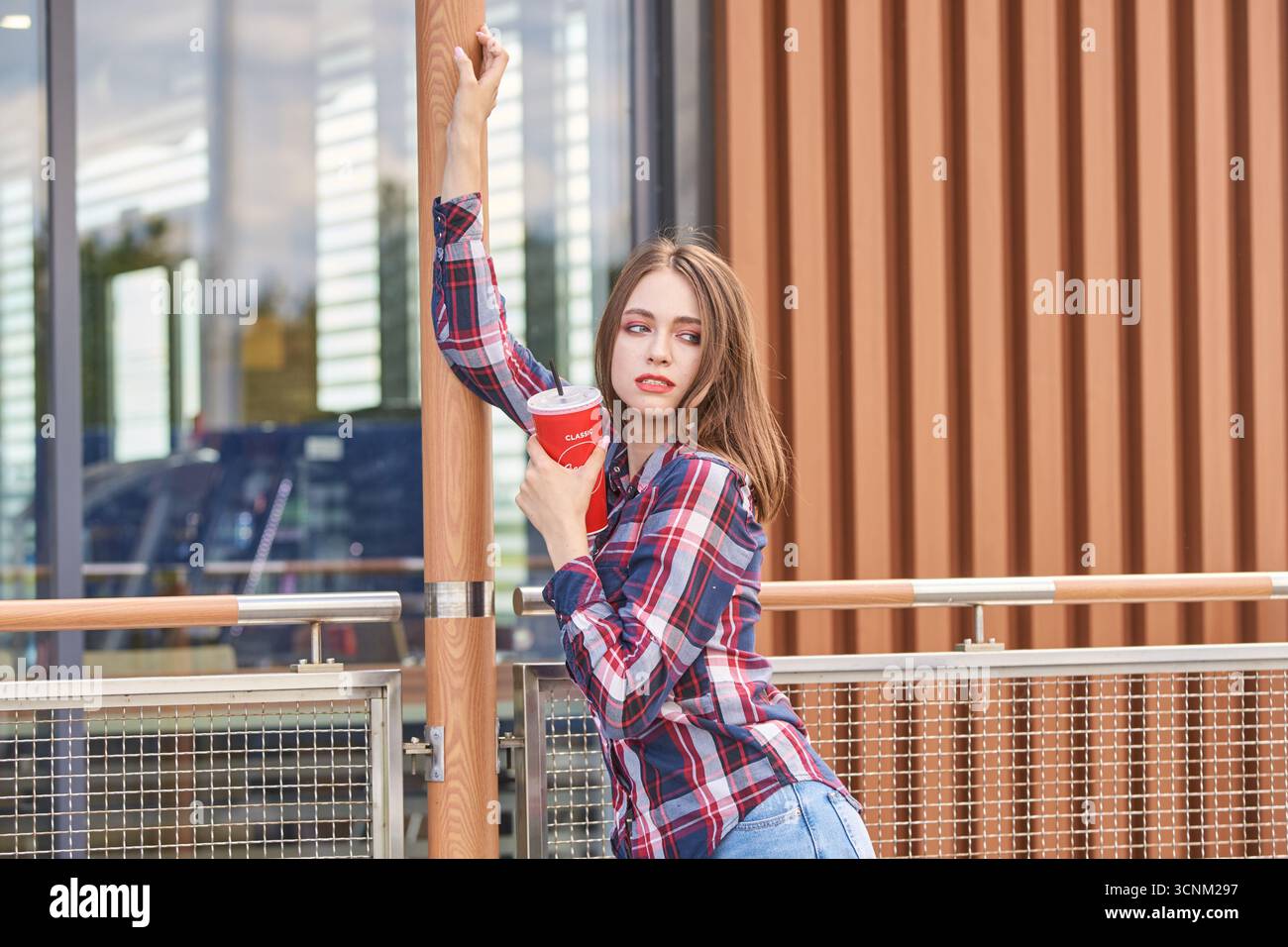 BARNAUL, SIBIRIEN, REGION ALTAI, RUSSLAND - 5. Juli 2019: Junge kaukasische Frau in kariertem Hemd mit großem Getränk im Freien in der Nähe eines modernen Gebäudes. Stockfoto