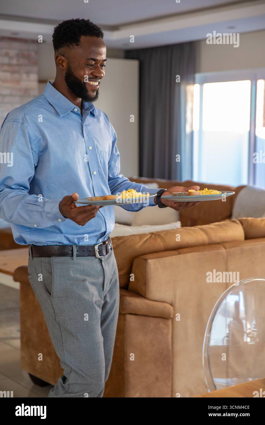 afroamerikaner mit zwei Tellern Rührei, Toast im Wohnzimmer, Kopierraum Stockfoto