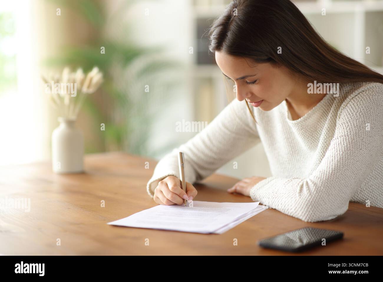 Frau unterschreibt Vertrag oder füllt Formular auf einem Holztisch in einem Zimmer zu Hause Stockfoto