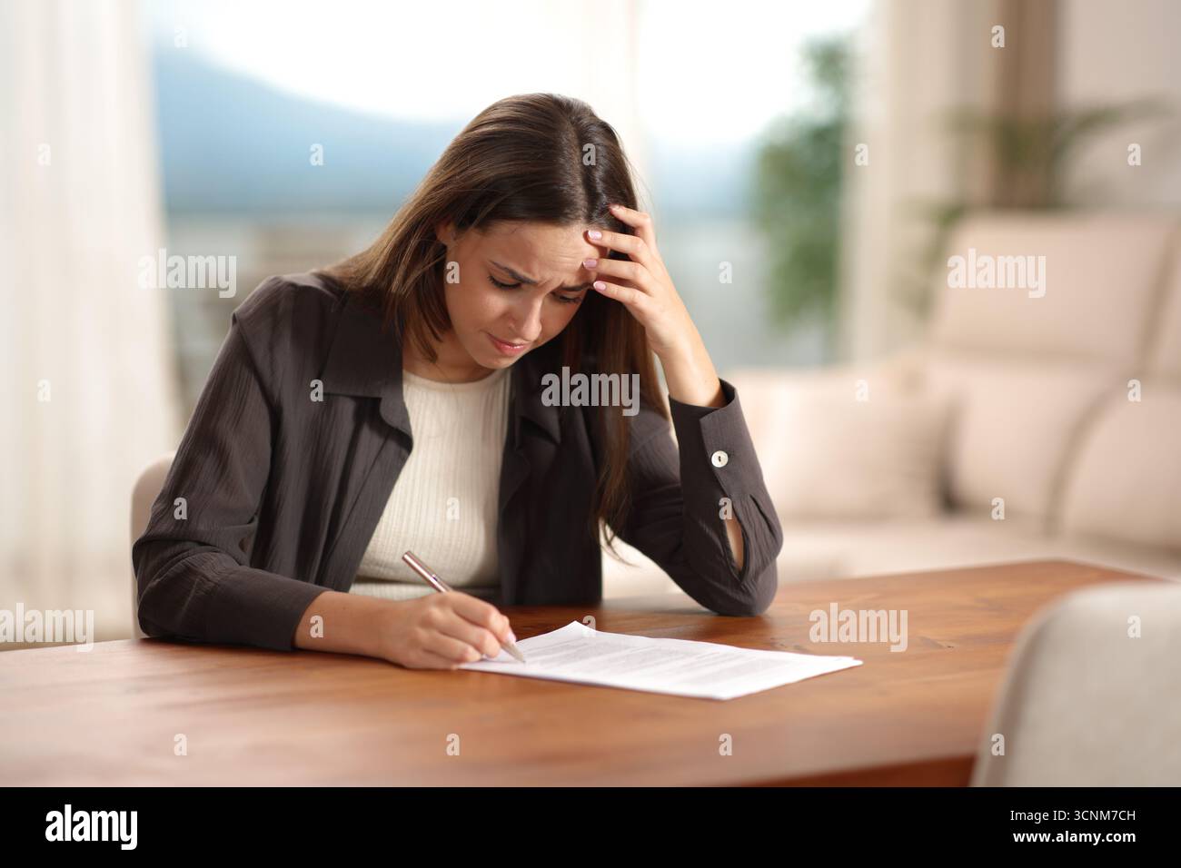 Besorgte Frau, die zu Hause einen Vertrag auf einem Holztisch unterschreiben will Stockfoto