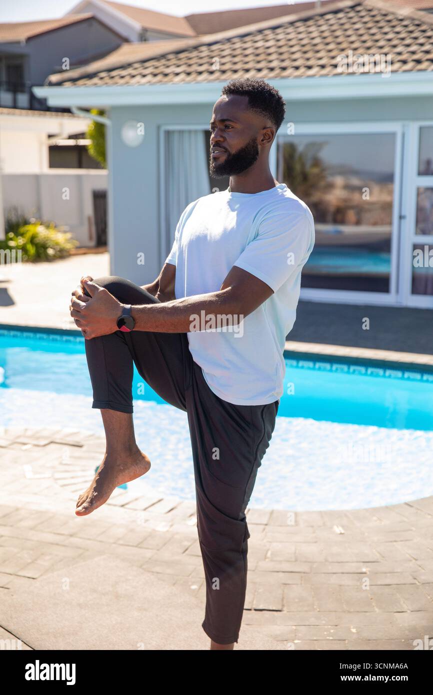 afroamerikaner, der sich von Knie bis Brust auf einer Steinterrasse neben dem Pool ausdehnt Stockfoto