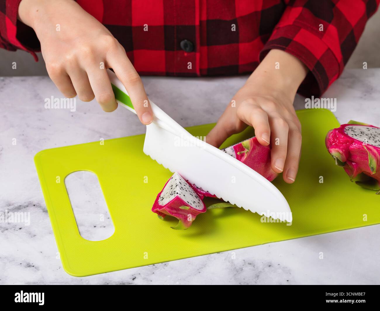 Ein Kind schneidet eine Drachenfrucht mit einem Plastikmesser auf einem grünen Schneidebrett Stockfoto