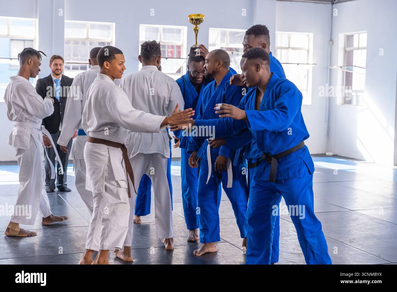Verschiedene männliche Kampfkünstler versammeln sich im Dojo, halten Goldtrophäe, während sie in blau-weißem gis gehalten werden Stockfoto