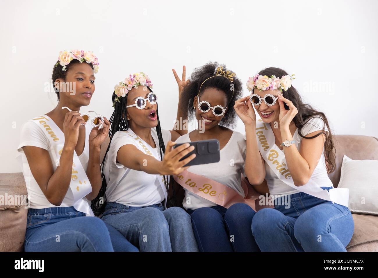 Verschiedene Freundinnen posieren für Selfie auf dem Sofa, tragen eine Schärpe und eine Sonnenbrille, während sie das Smartphone halten Stockfoto