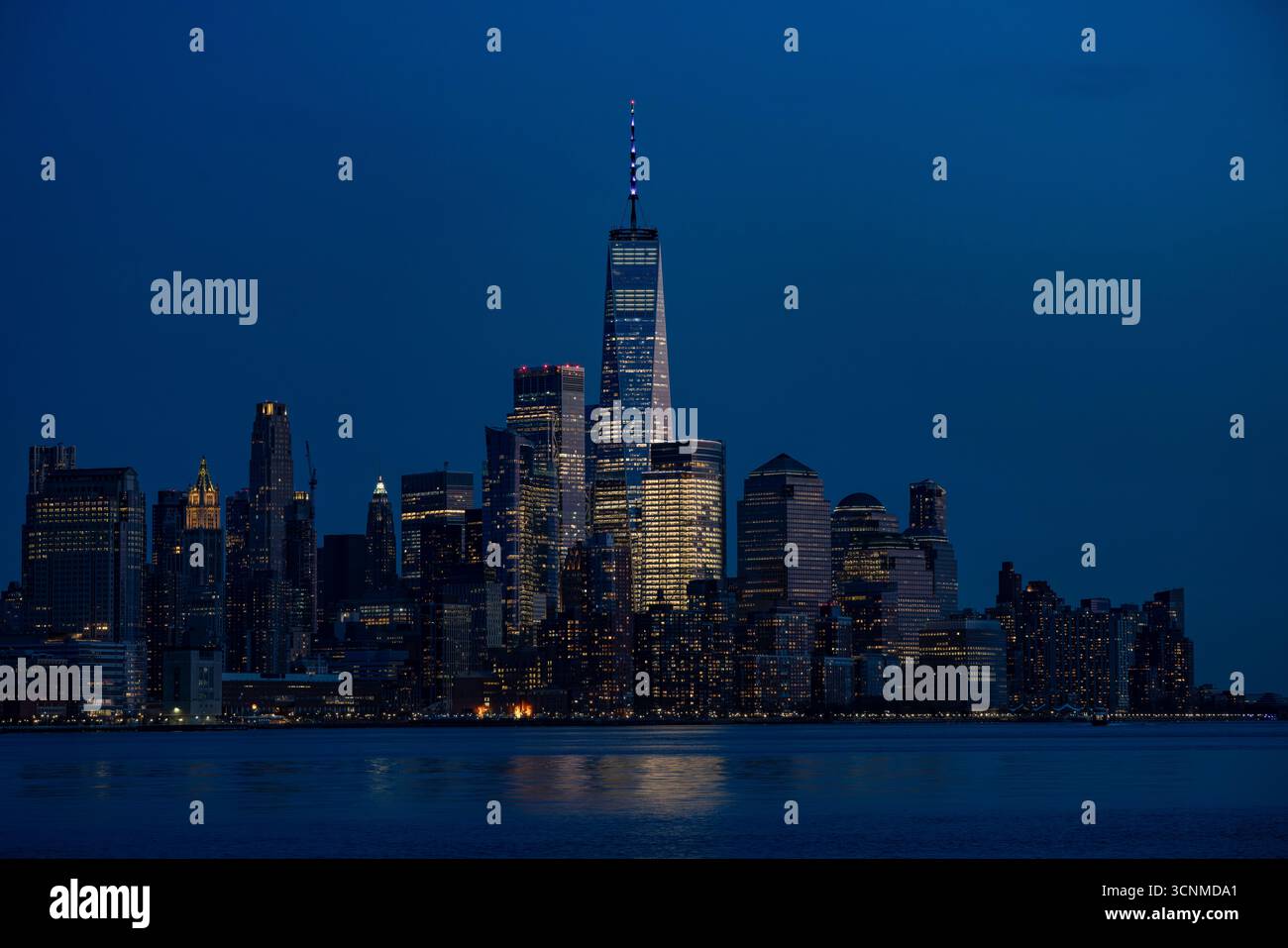 Blick auf die Skyline der Stadt mit hoch aufragenden Wolkenkratzern, die das verblassende Licht der Dämmerung über dem ruhigen Wasser reflektieren, New York, USA. Stockfoto