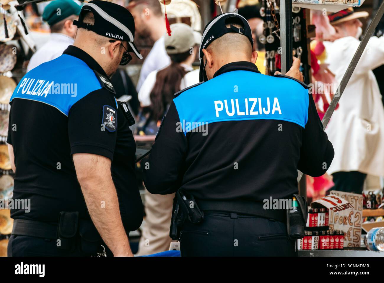 Marsaxlokk, Malta - 13. April 2025: Zwei maltesische Polizeibeamte in Uniformen mit Pulizija-Insignia patrouillieren auf dem geschäftigen Sonntagsmarkt im Fischi Stockfoto