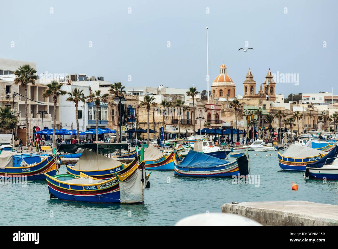 Marsaxlokk, Malta - 13. April 2025: Traditionelle, farbenfrohe maltesische Fischerboote, genannt Luzzu, mit leuchtend blauen, gelben und roten Details, die in der verankert sind Stockfoto