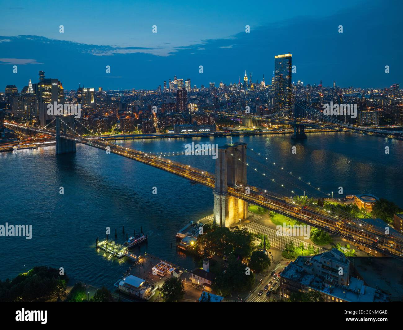Die beleuchtete Brooklyn Bridge aus der Vogelperspektive erstreckt sich über den East River und verbindet die glitzernde Skyline von Manhattan unter der verblassenden Dämmerung in Manhattan, New York, USA. Stockfoto