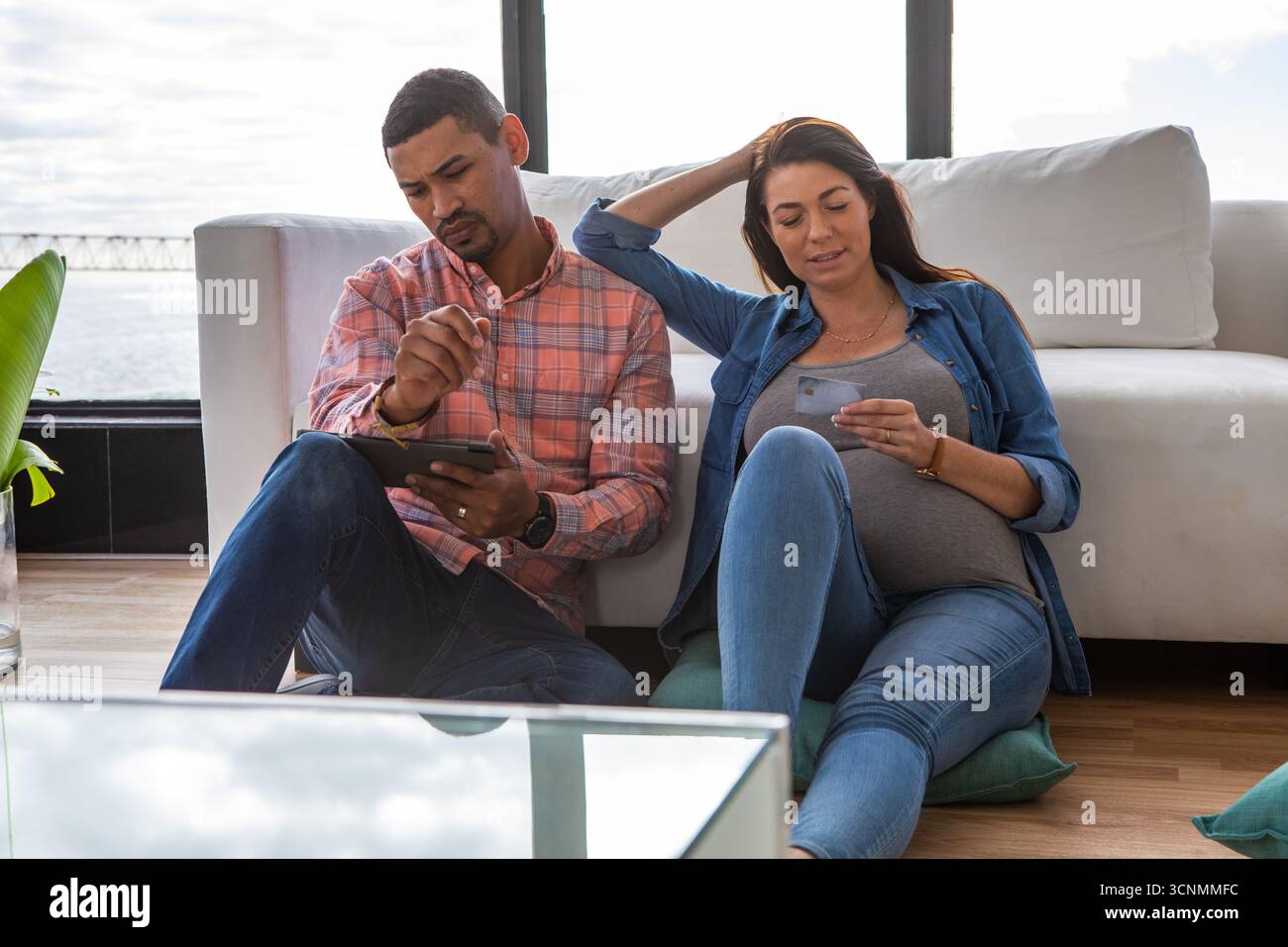 Verschiedene Freundinnen sitzen auf Kissen im Wohnzimmer und halten den Stift Kreditkarte mit Tablet Stockfoto