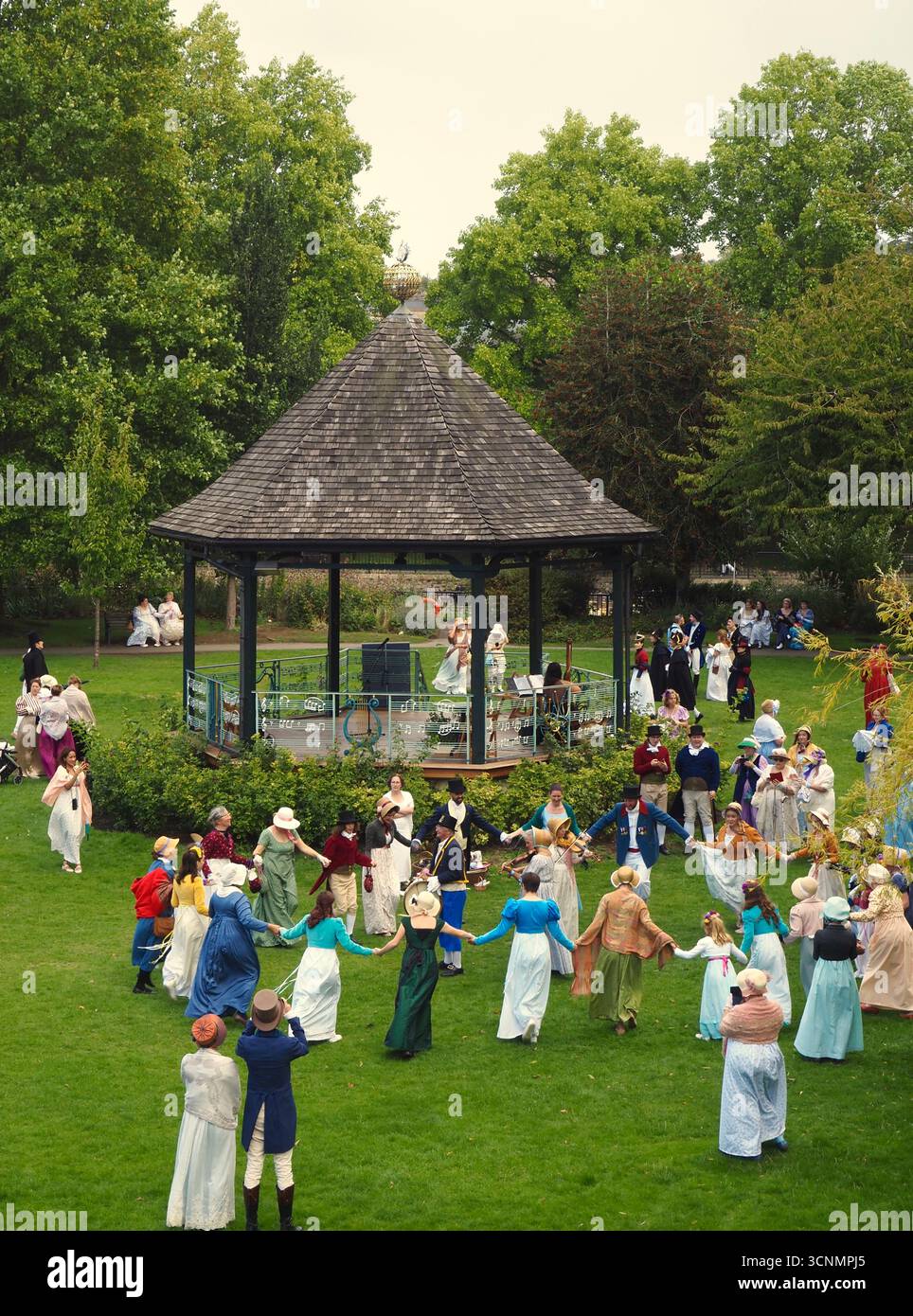 Die in Regentalkostümen gekleideten Menschen bereiten sich auf einen traditionellen Tanz im Parade Gardens Bath bei der Jane Austen Festival Parade 2025 vor. Stockfoto