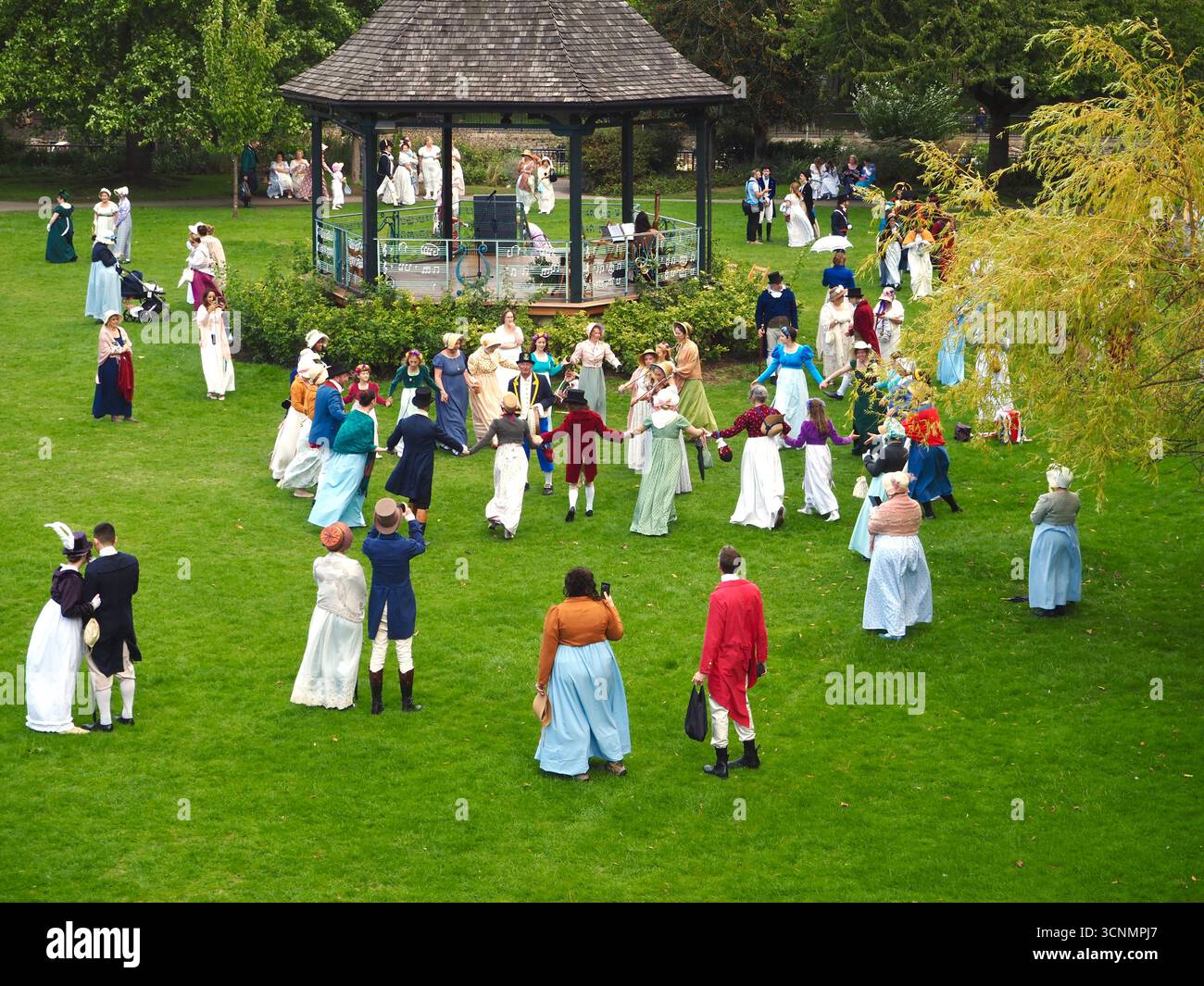 Die in Regentalkostümen gekleideten Menschen bereiten sich auf einen traditionellen Tanz im Parade Gardens Bath bei der Jane Austen Festival Parade 2025 vor. Stockfoto
