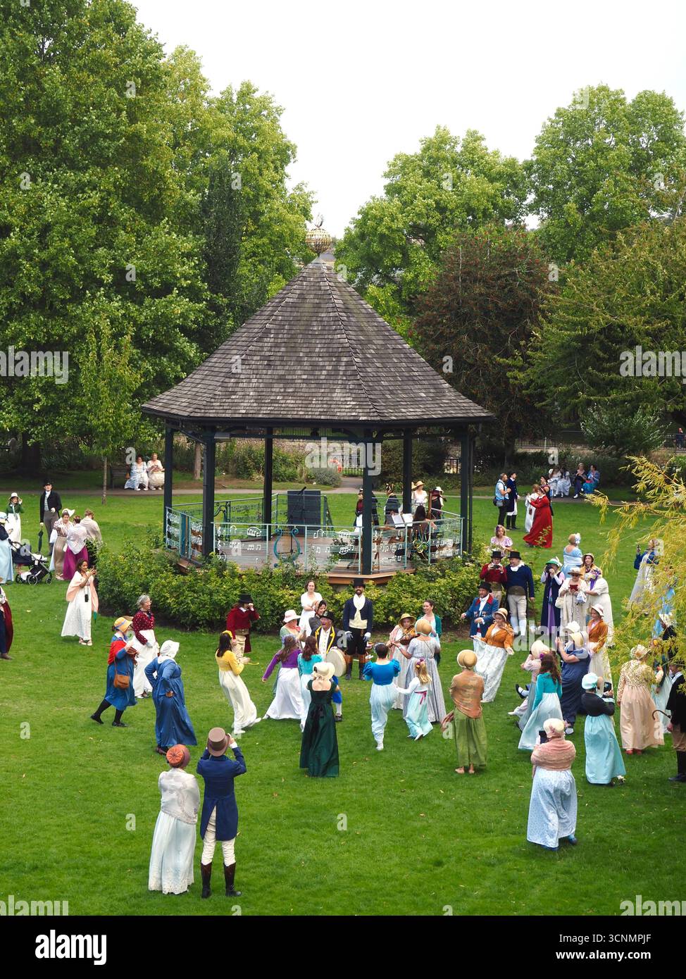 Die in Regentalkostümen gekleideten Menschen bereiten sich auf einen traditionellen Tanz im Parade Gardens Bath bei der Jane Austen Festival Parade 2025 vor. Stockfoto