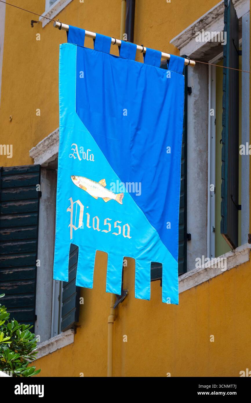 Blaue Flagge vor dem gelben Gebäude in einer engen Straße in der Altstadt von Gardasee, Verona, Italien Stockfoto