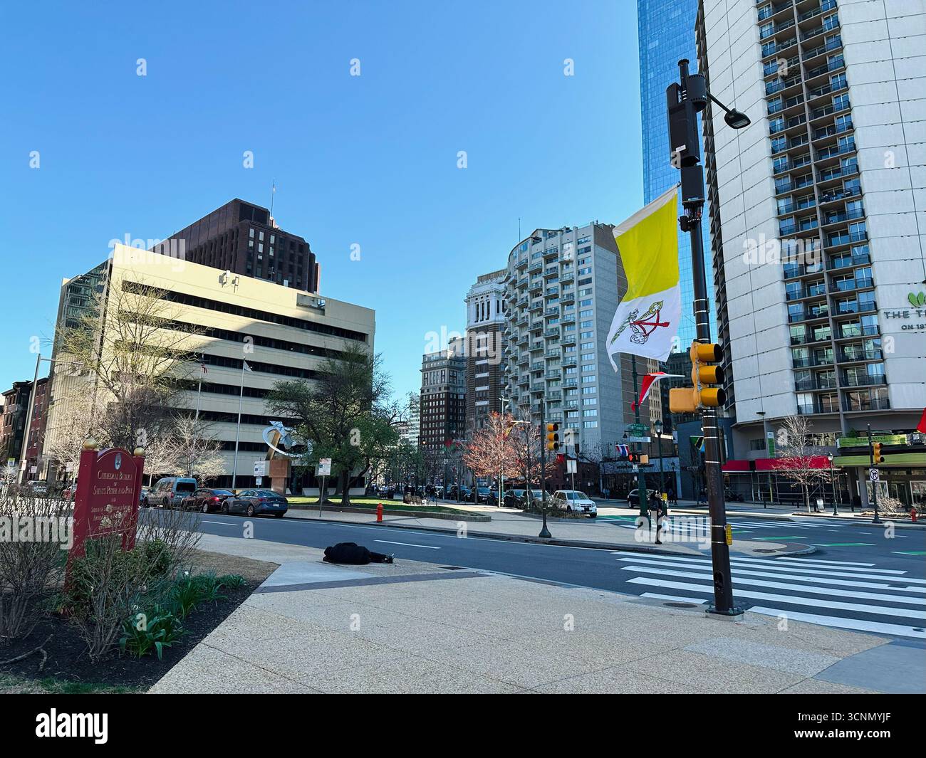 Philadelphia, Pennsylvania, USA - 29. April 2025: Eine belebte Straße in Philadelphia mit Hochhäusern, Vatikanflagge und hellblauem Himmel. Stockfoto