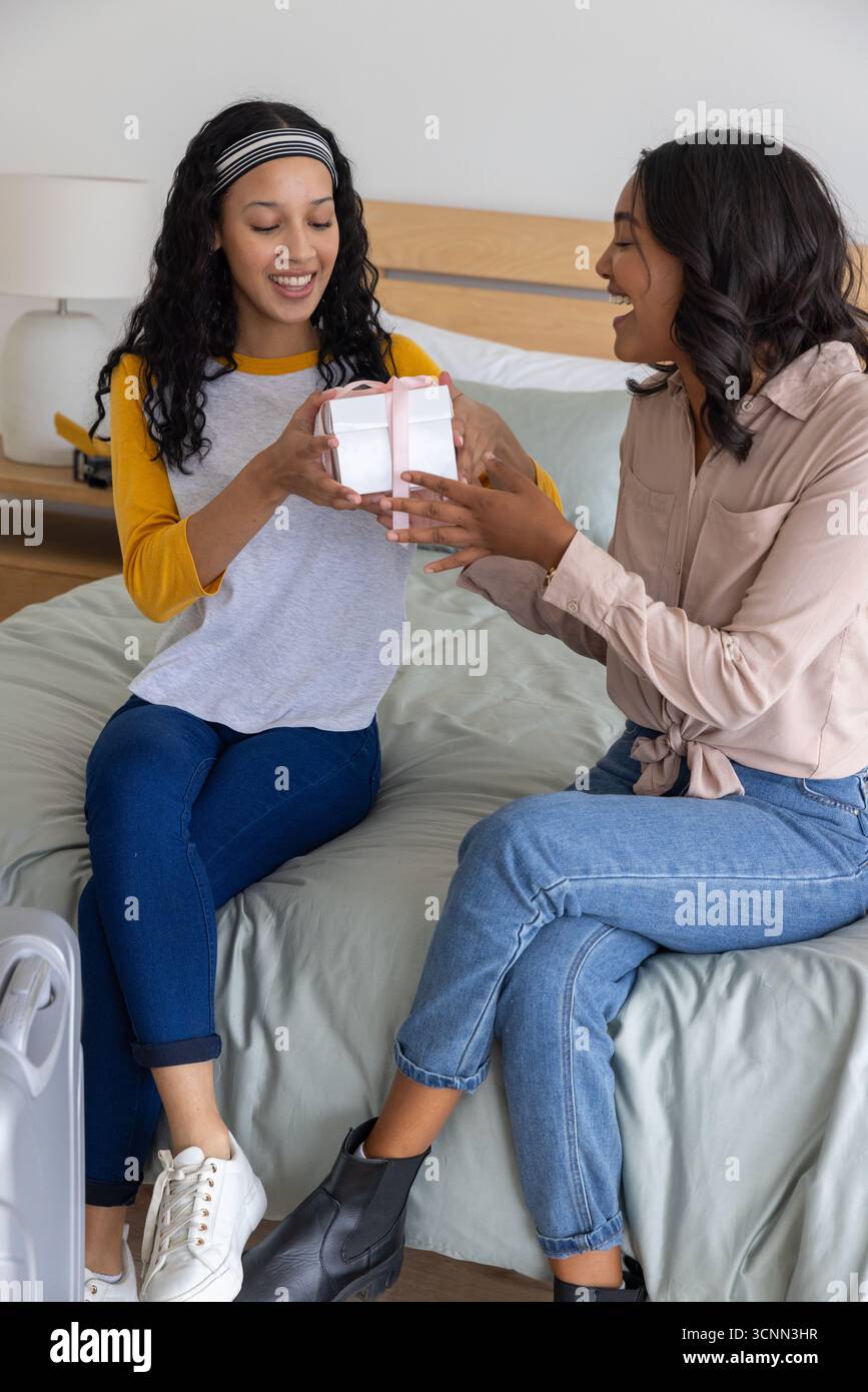 Verschiedene Eltern und Teenager-Tochter überreichen kleine weiße Geschenkbox mit rosa Schleife im Schlafzimmer Stockfoto