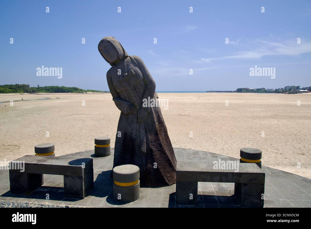 Aus nächster Nähe sehen Sie eine weibliche Gestalt aus Stein auf einem kleinen platz am Pyoseon Beach, mit Bänken und den riesigen Wattflächen, die sich bis zum Meer erstrecken. Stockfoto