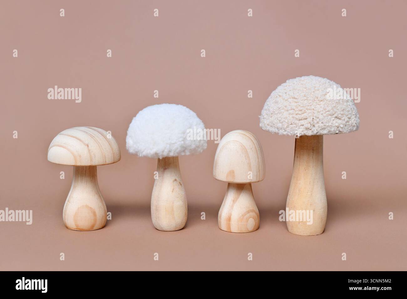 Vier hölzerne Pilzornamente hintereinander auf beigefarbenem Hintergrund Stockfoto