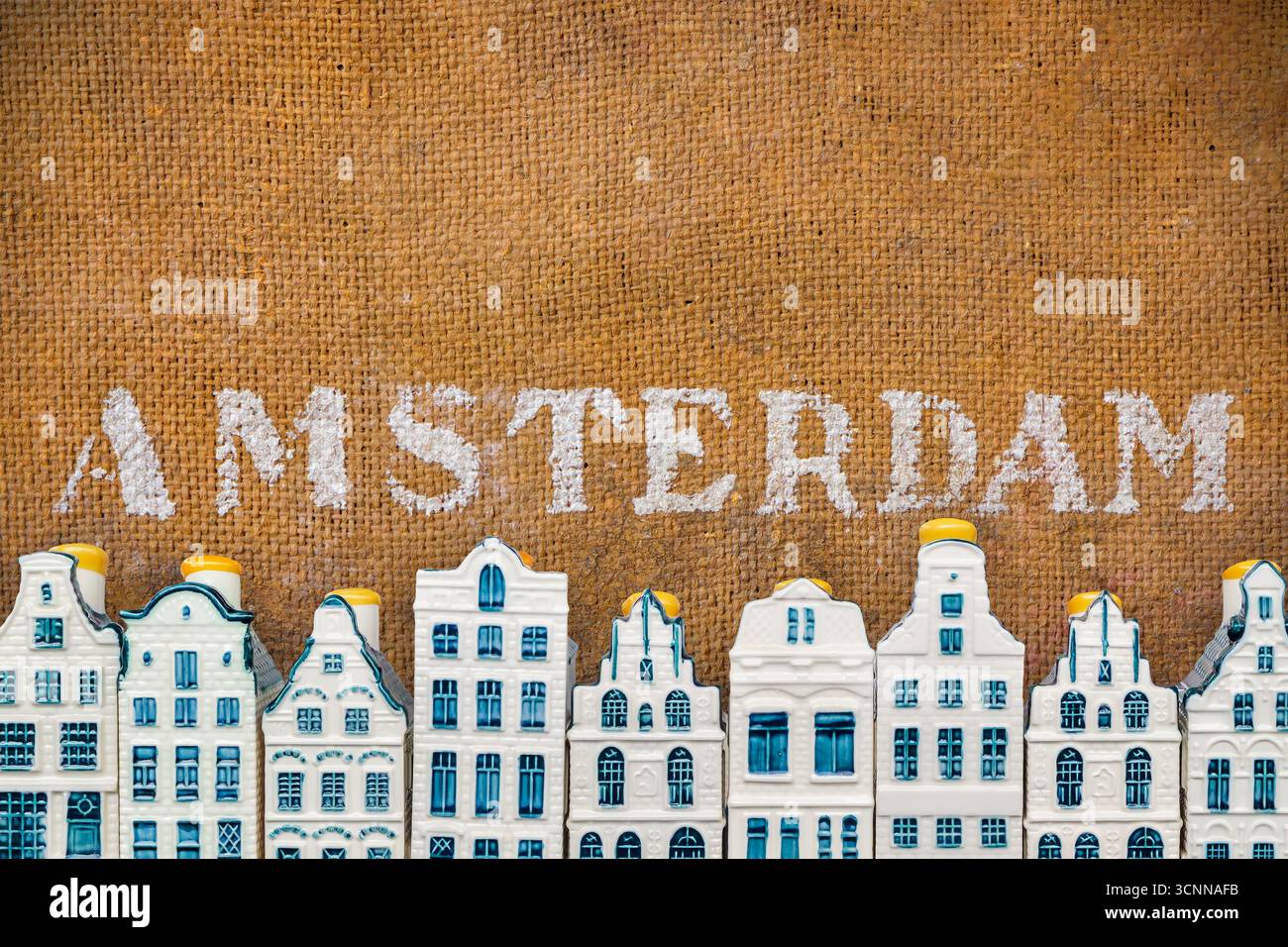 Reihe von blauen Miniatur-Souvenir-Porzellan-Kanalhäusern vor einem alten braunen Hintergrund mit dem Text Amsterdam Stockfoto