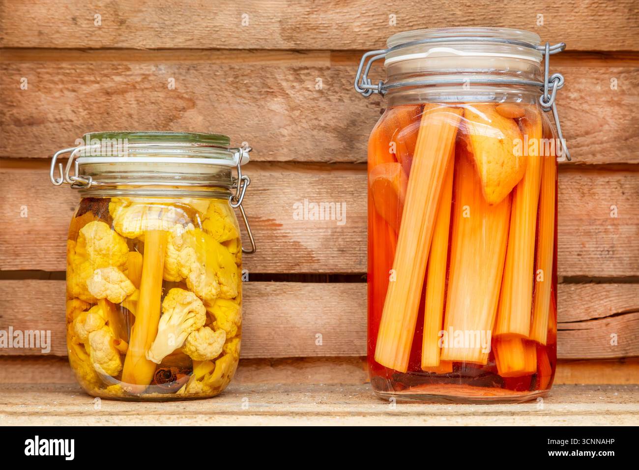 Zwei Glaskonserven mit konserviertem Gemüse vor einer Holzwand Stockfoto