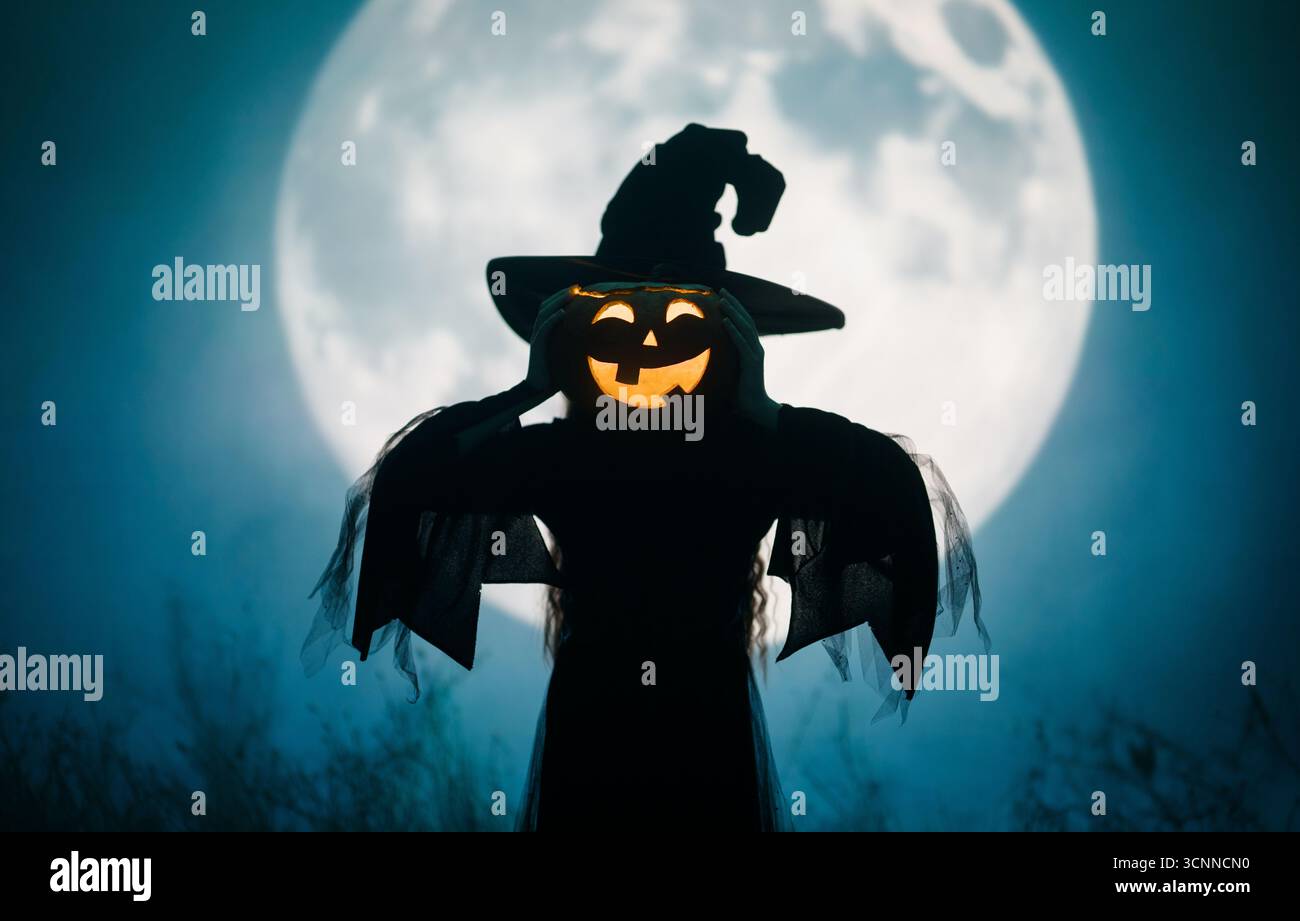 Mädchen in Hexenkostümen für Halloween. Junge, der auf Vollmond-Hintergrund steht. Stockfoto