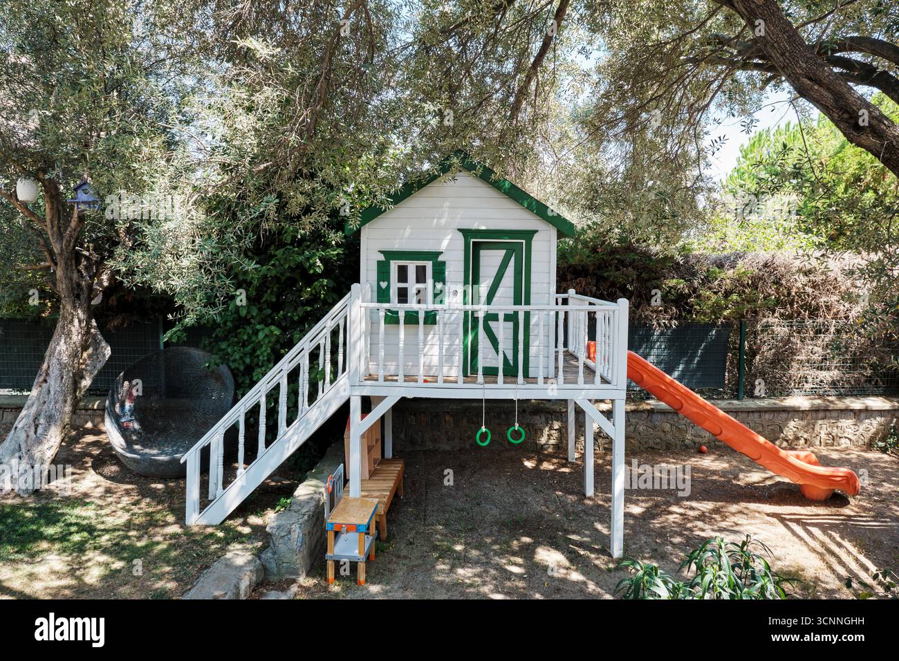 Kinderspielhaus mit Rutsche und Turnringen in einem von Olivenbäumen beschatteten Garten, in dem Kinder spielerisch und sicher spielen können Stockfoto