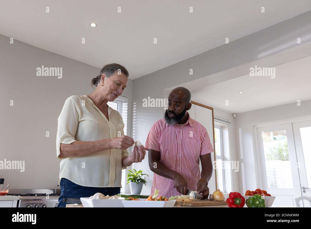 Verschiedene Paare, die Paprika, Zwiebeln und Eier in eine Schüssel auf der Kücheninsel hacken Stockfoto