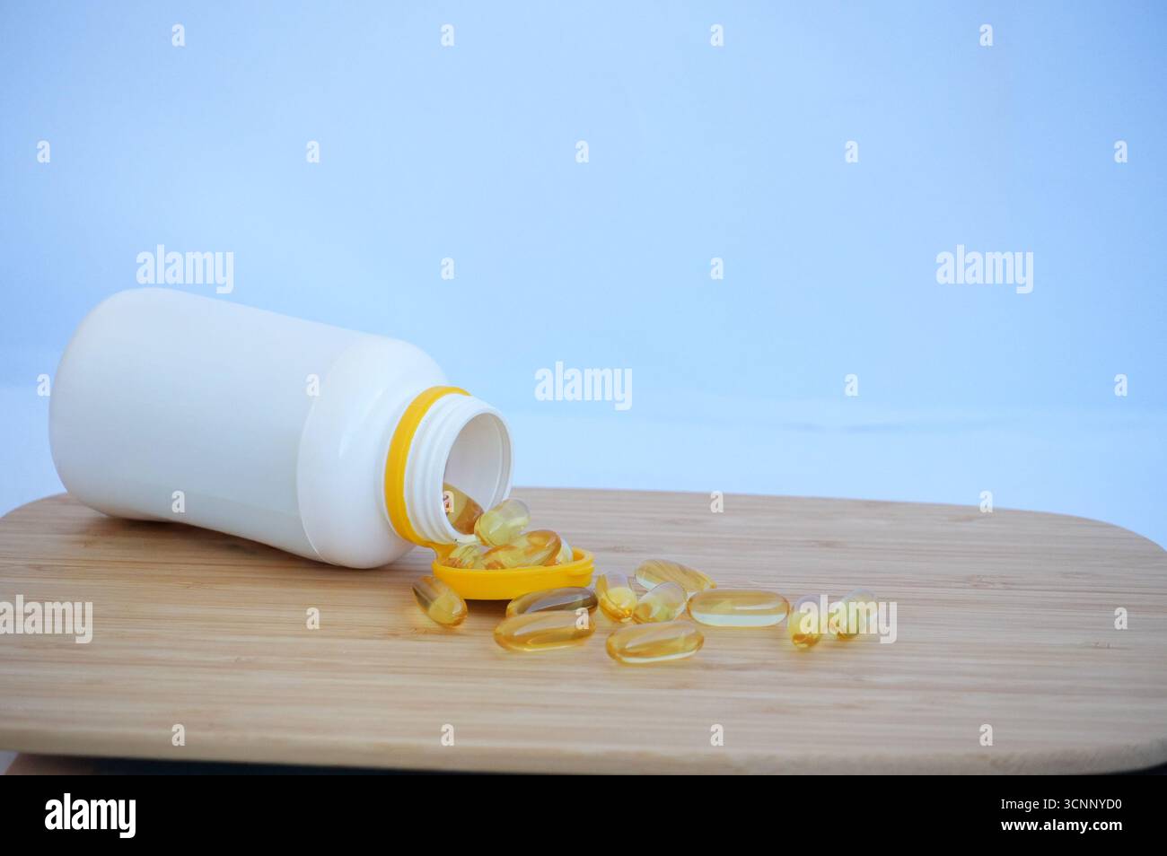 Fischöl Kapseln auf Holzbrett und weiße Flasche auf blauem Hintergrund Stockfoto