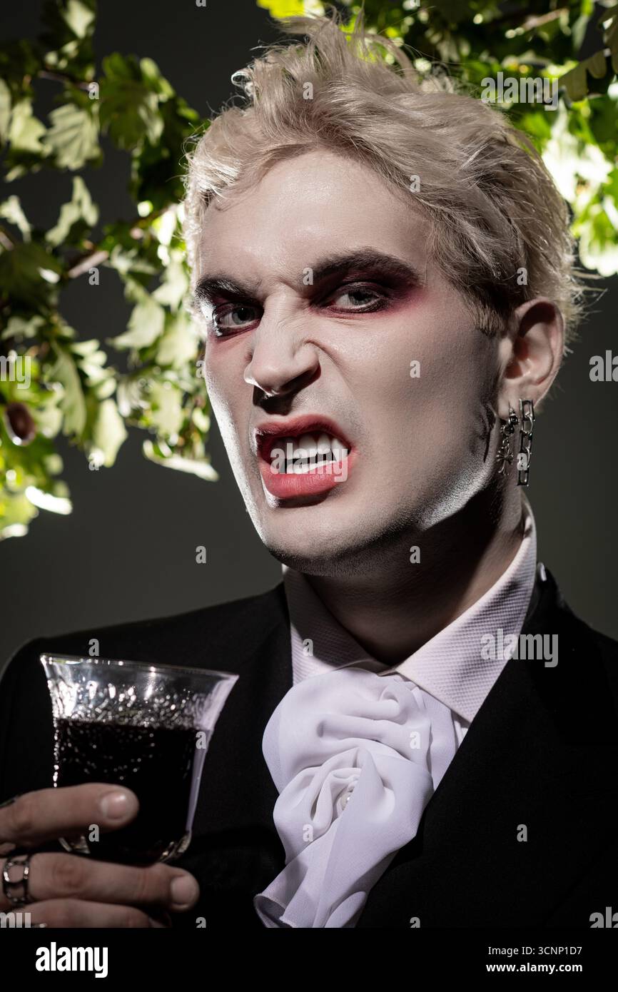 Ein junger Mann zeigt Kreativität mit einem epischen Halloween-Kostüm, auffälligem Make-up und einem lustigen Drink. Stockfoto
