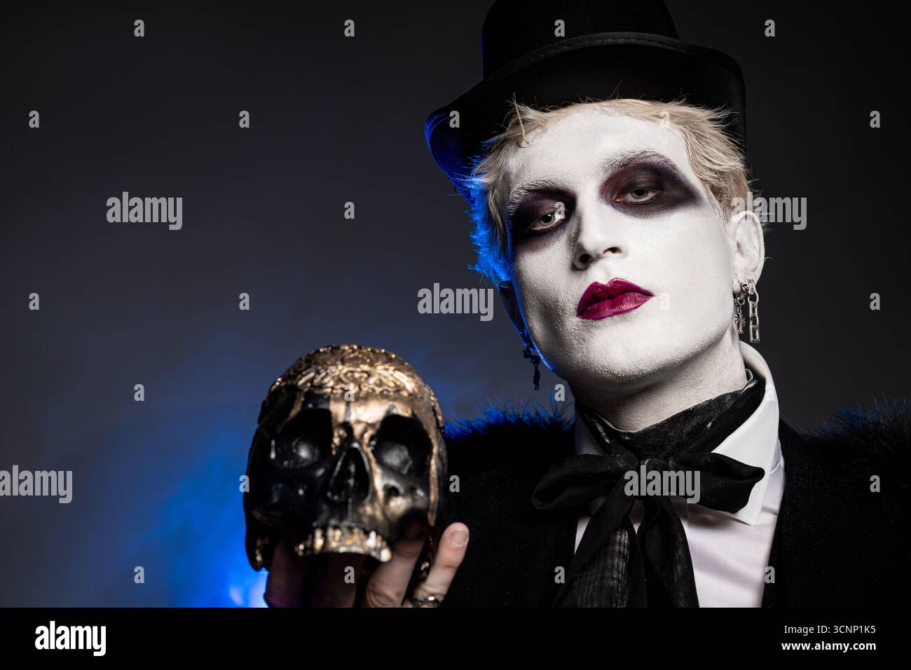 Ein hübscher junger Mann trägt eine auffällige Halloween-Verkleidung und hält einen dekorativen Schädel zur Feier. Stockfoto