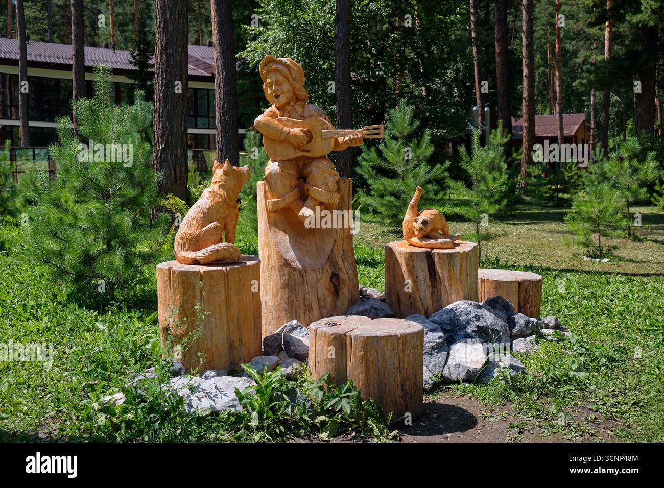 Park Hotel Podgorica, Altai, Russland - 11. Juli 2024: Festival der Holzskulpturen in Altai. Holzgeschnitzte Figur eines Mannes, der Gitarre spielt, mit einem Fuchs und einem C. Stockfoto