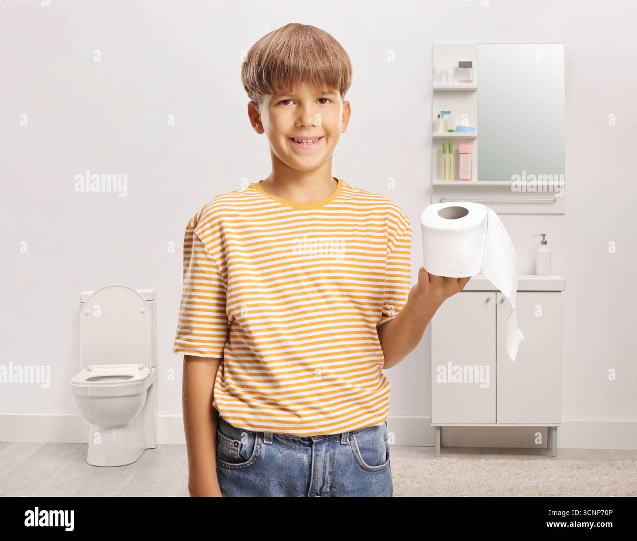 Ein Junge, der eine Toilettenpapierrolle im Badezimmer hält Stockfoto