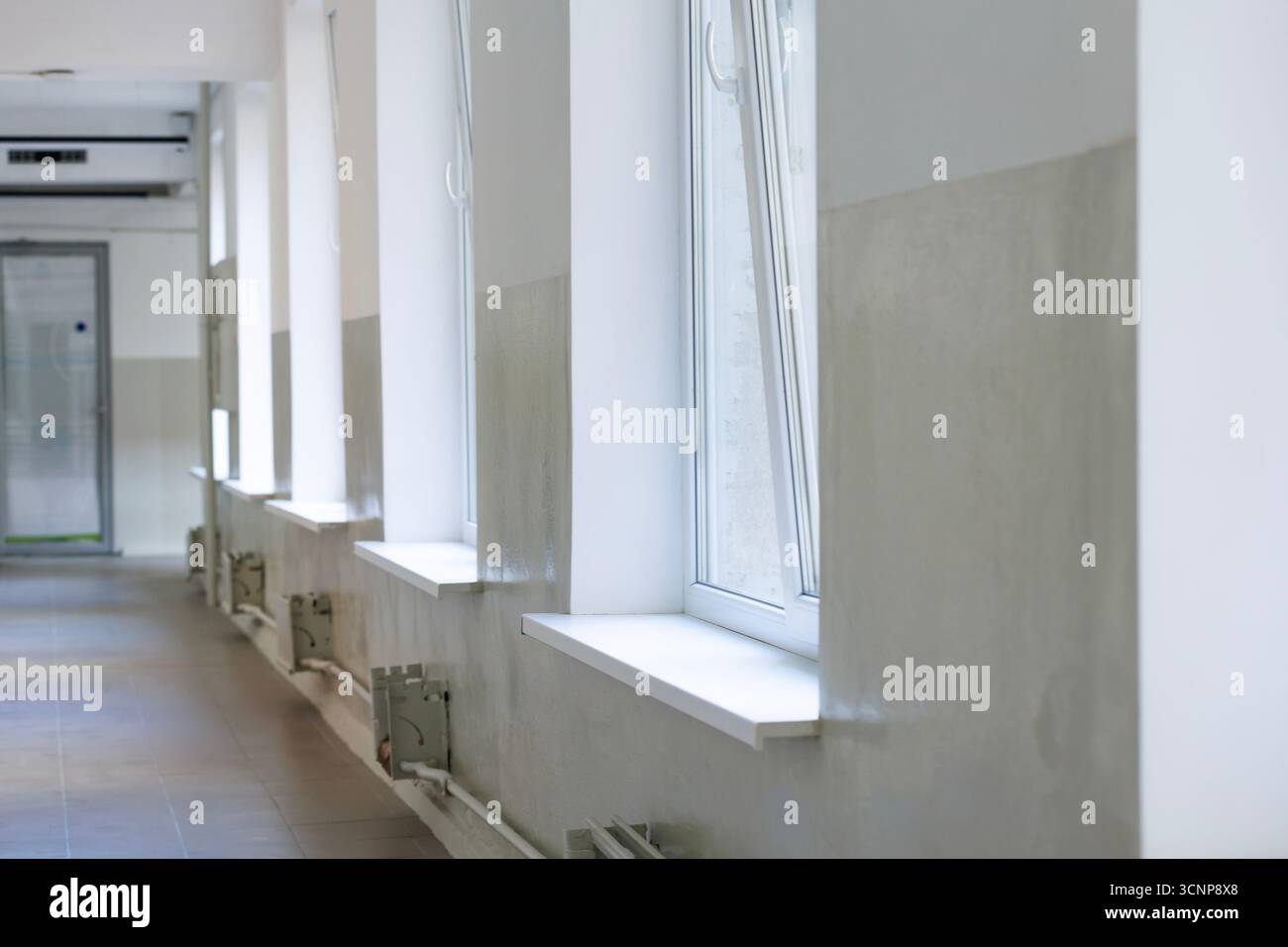 Langer gefliester Korridor. Leerer Flur mit hohen Fenstern, die Tageslicht hereinlassen. Stockfoto