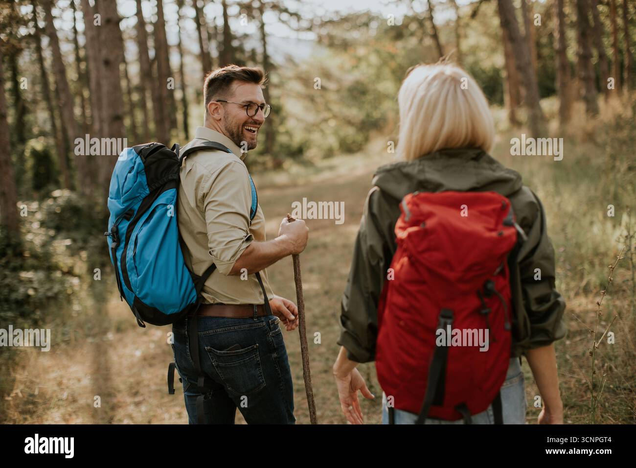 Ein Mann und eine Frau wandern auf einem üppigen Waldweg, plaudern und lächeln. Die Sonne zieht durch die Bäume und schafft eine warme und einladende Atmosphäre für die Th Stockfoto