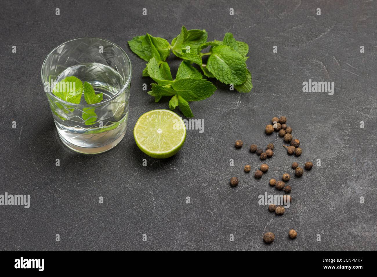 Glas Wasser und Minze. Halbe Limette und Minzzweige auf dem Tisch. Schwarzer Hintergrund. Draufsicht. Stockfoto