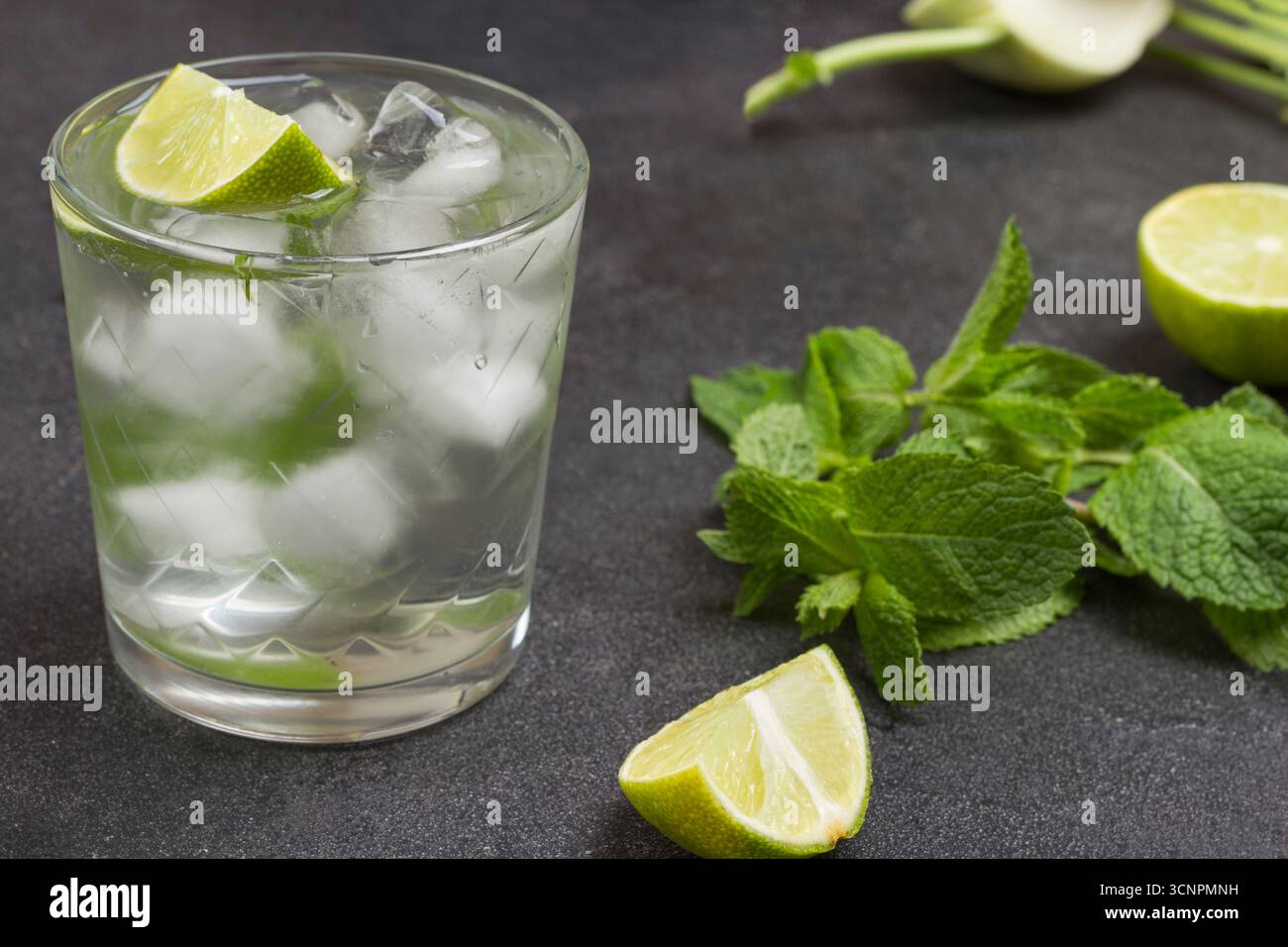 Beschlagenes Glas mit Kalk und Eis. Minzzweige und Limettenhälften auf dem Tisch. Schwarzer Hintergrund. Draufsicht Stockfoto