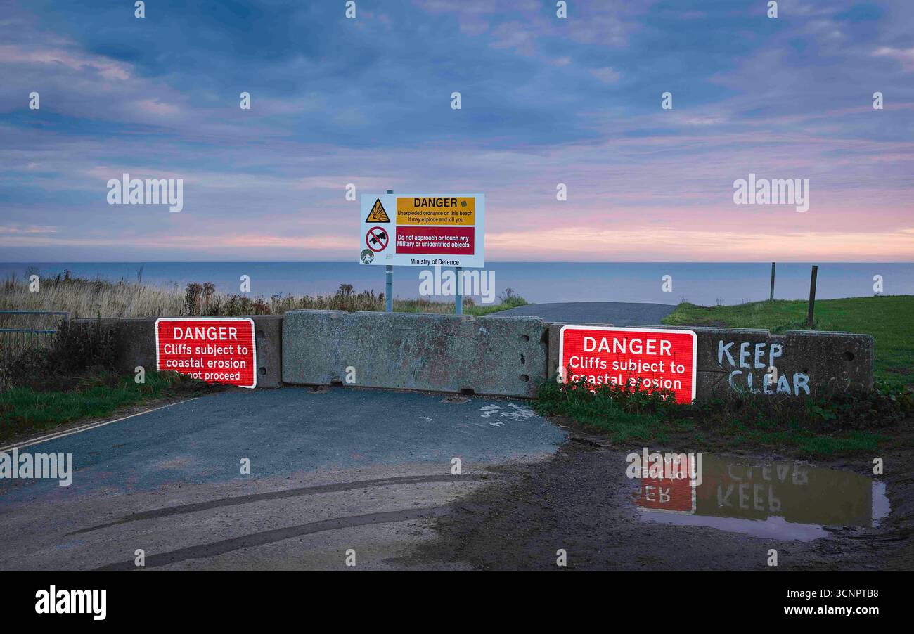 Reflektierende, farbenfrohe Warnzeichen für schwere Küsten- und Straßenerosion sowie Gefahrenzeichen für nicht explodierte Kampfmittel aus dem vergangenen Weltkrieg. Aldbrough. Stockfoto