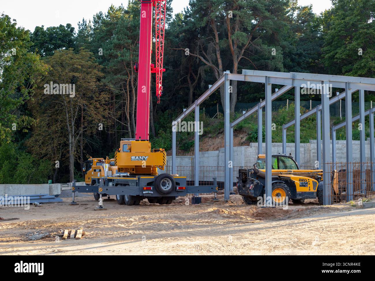 Mobilkran und Teleskoplader auf einer Baustelle eines Gebäudes im Bau nach der Arbeit. Der Rahmen eines Gebäudes, das sich im Bau befindet Stockfoto
