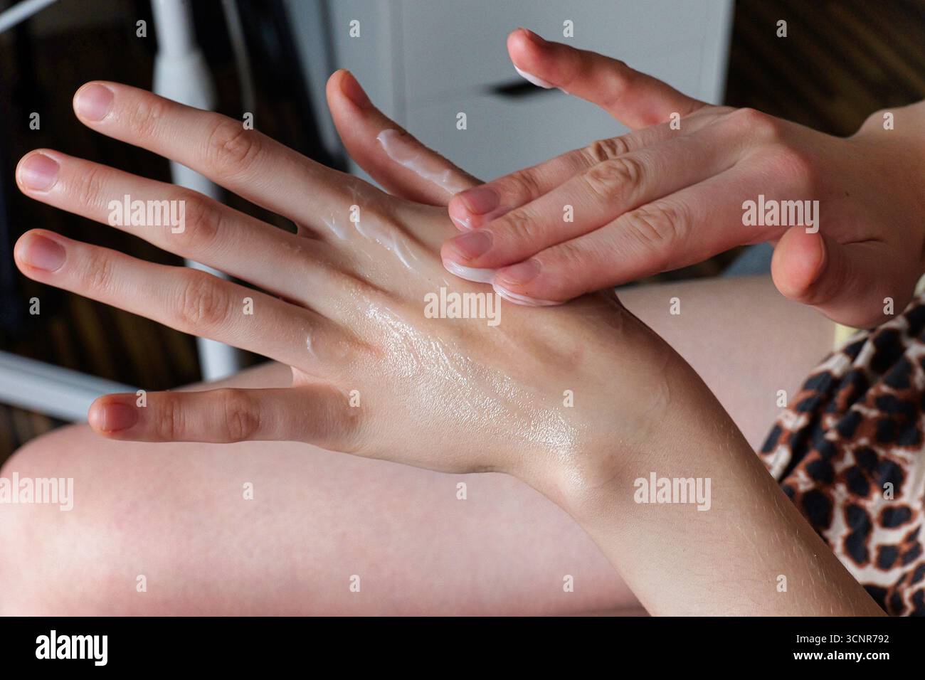 Sanfte Hände, die die weiße Feuchtigkeitscreme in eine glatte Handgelenkhaut einreiben, in gemütlicher Innenumgebung Stockfoto
