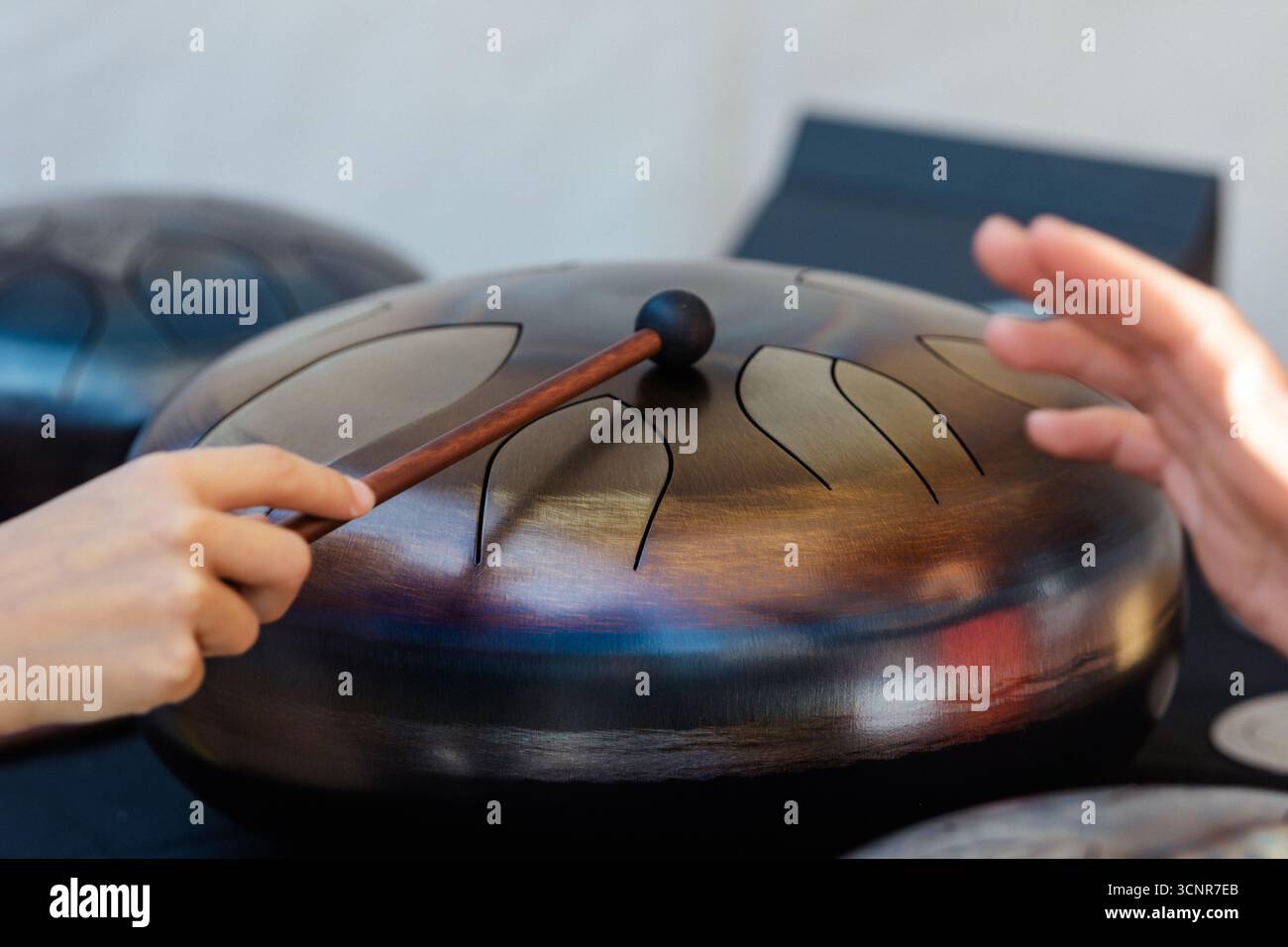 Hände, die mit einem Hammer eine Stahlzungentrommel spielen. Nahaufnahme eines melodischen Percussionsinstruments, das in Meditation, Yoga, Klangtherapie und Entspannung eingesetzt wird Stockfoto