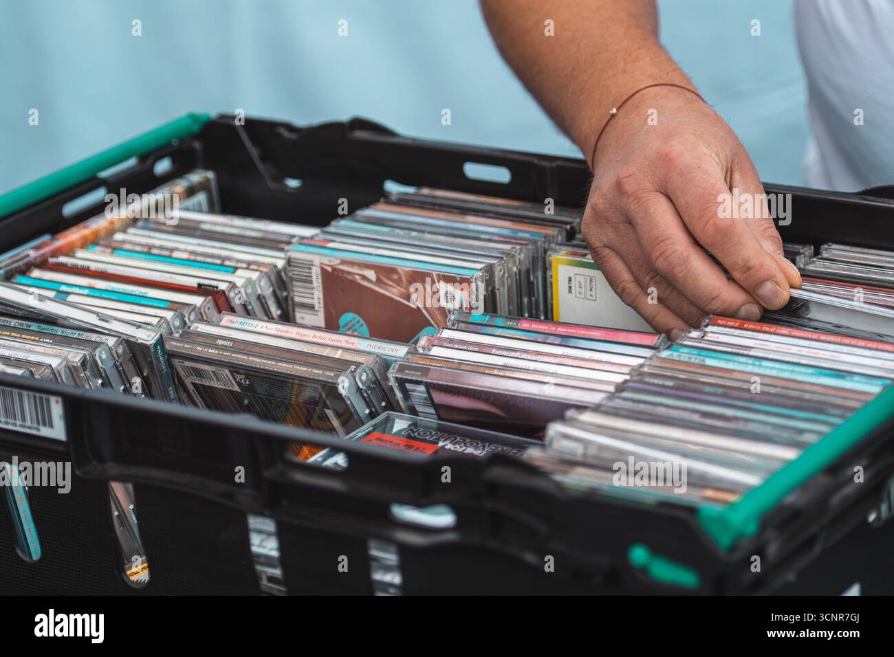 Nahaufnahme eines Mannes, der CDs in einer Plastikkiste auf einem Markt oder einem Musikgeschäft durchsucht. Handsuche durch CDs, die Retro-Musikformate darstellen Stockfoto