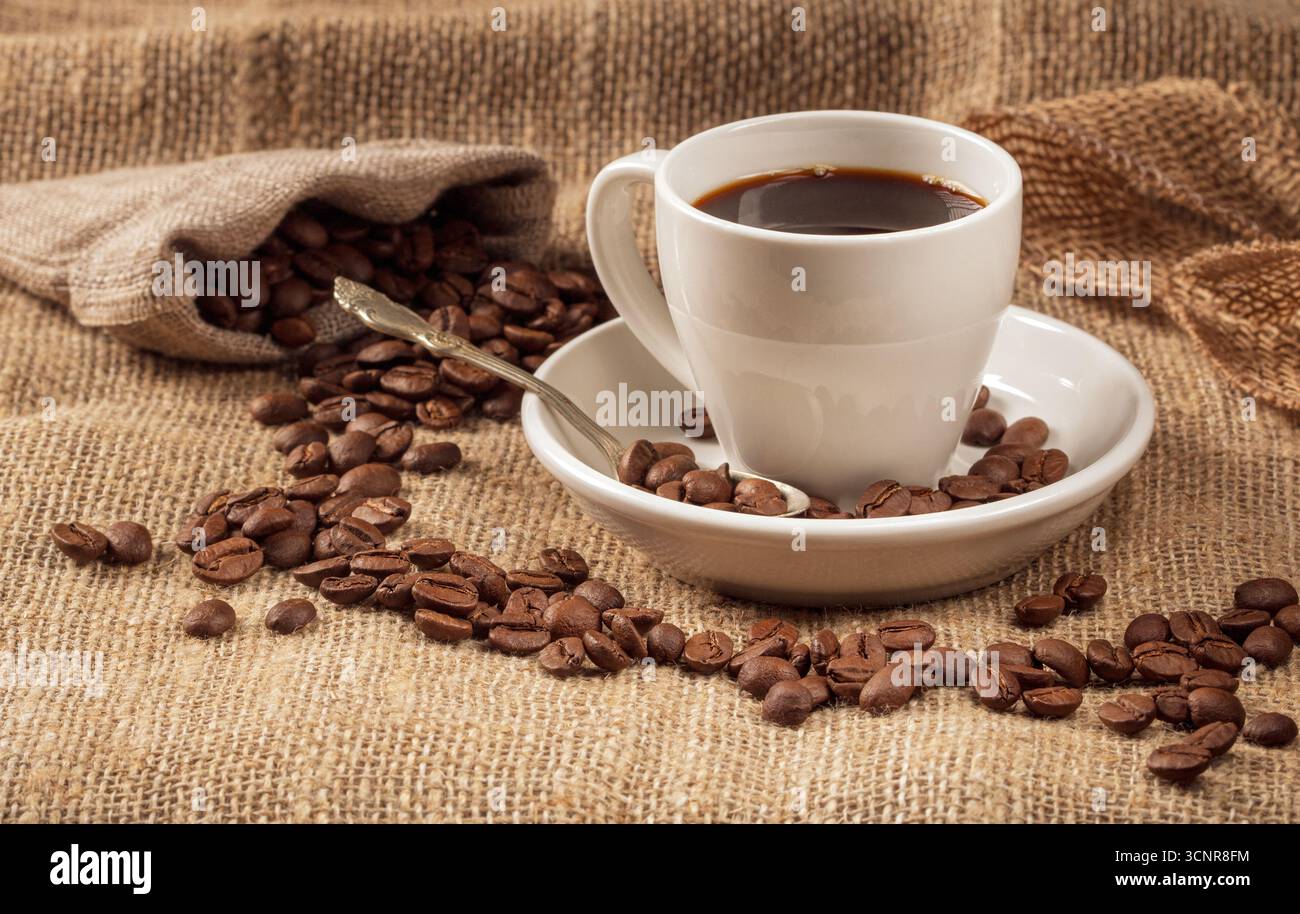 Eine warme und einladende Kaffeeszene mit einer wunderschön gefertigten Tasse Kaffee, umgeben von kräftigen Kaffeebohnen, alles gegen eine strukturierte Rückseite Stockfoto
