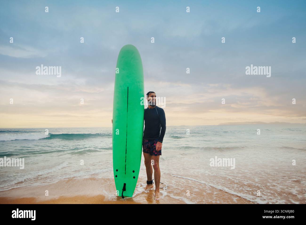 Bärtiger Mann mit Surfbrett in der Nähe eines Strandes. Mann mit Surfbrett im Freien an einem Sommertag Stockfoto