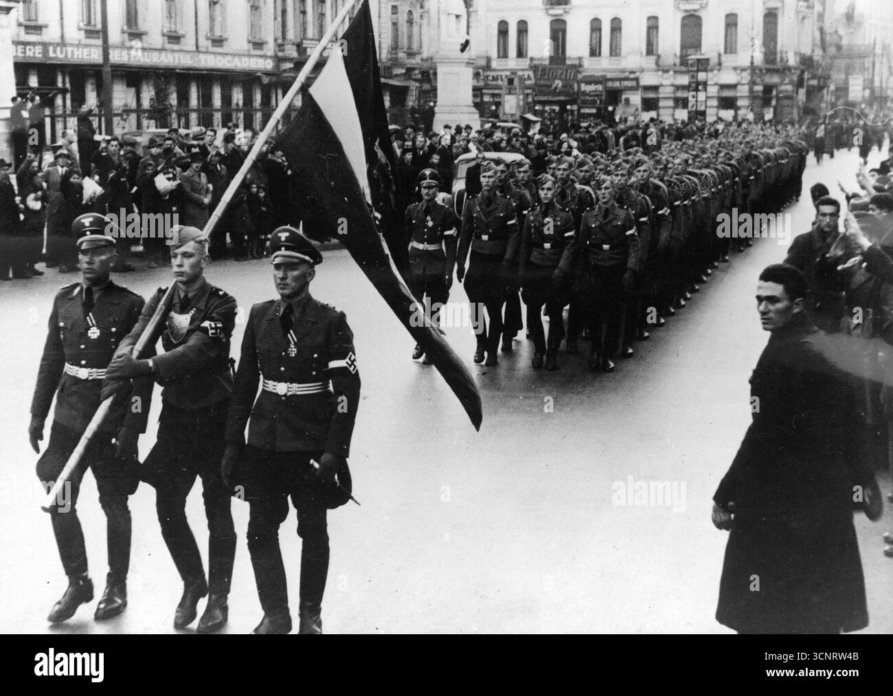 Eine Hitlerjugend-Delegation marschiert durch die Straßen von Bukarest. Ein Bannerwächter führt den Weg. Die Bewohner der Stadt beobachten den marsch. 1940 Stockfoto