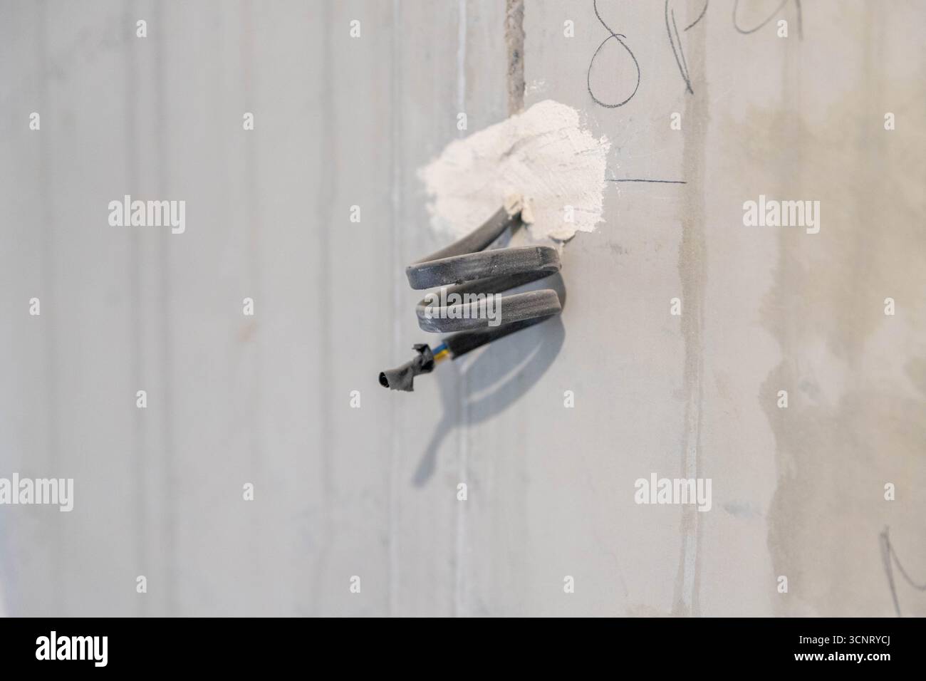 Kabel, die aus der grauen Betonwand ragen. Details während der Renovierung des Hauses. Stockfoto