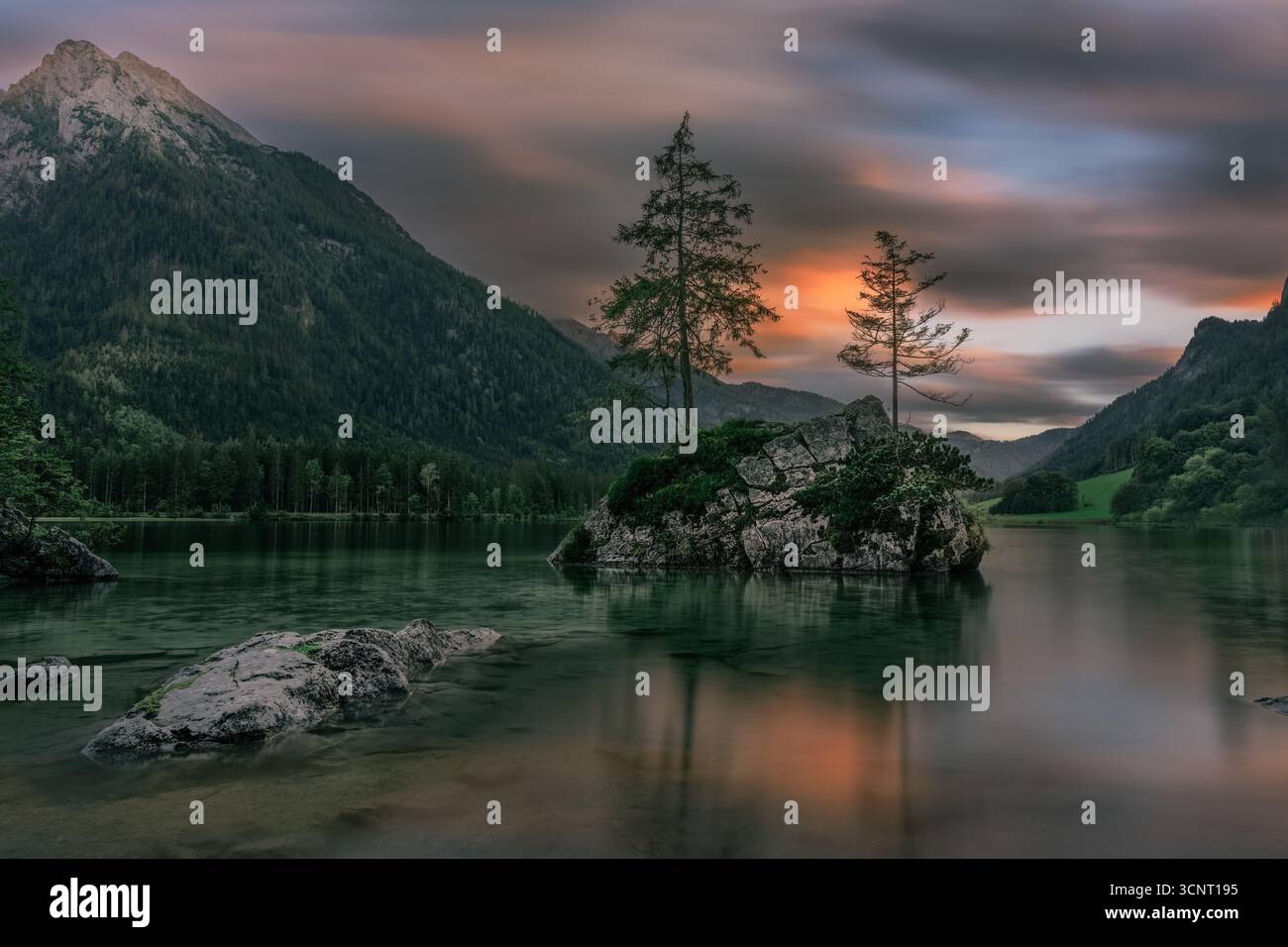 Ruhiger Bergsee mit Bäumen auf Rock Island bei Sonnenuntergang in malerischer Alpenlandschaft – ruhige Natur und Blick auf Reflexion Stockfoto
