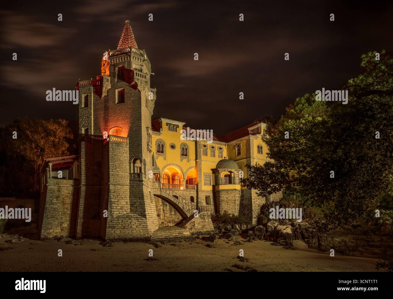 Beleuchtete historische Burgarchitektur in Portugal bei Nacht mit dramatischem Himmel, Steinmauern und glühenden warmen Lichtern Stockfoto