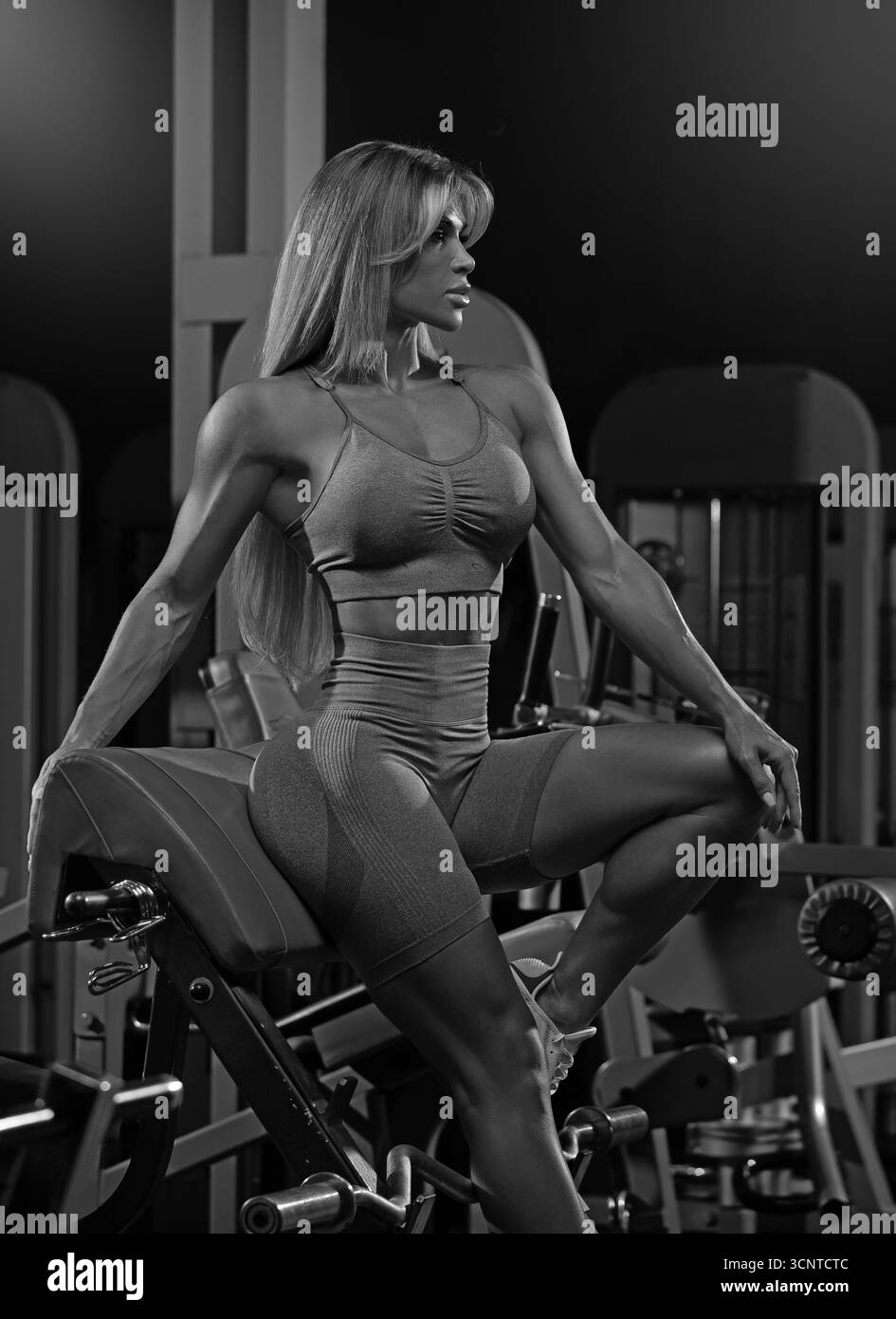 Die blonde Frau ist abends in einem Fitnessstudio mit Krafttraining beschäftigt. Sie nutzt Fitnessgeräte, um ihre Fitness zu verbessern und zeigt ihr Engagement für die Gesundheit. Stockfoto