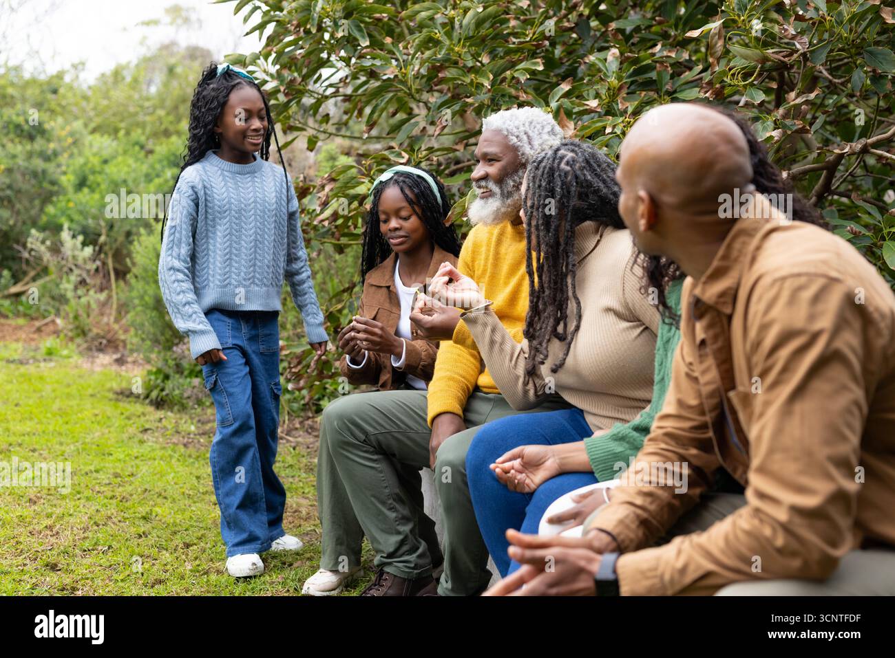 Afroamerikanische Familie trifft sich auf Holzbank im Park, plaudert und bewundert Sneakers und Zweige Stockfoto